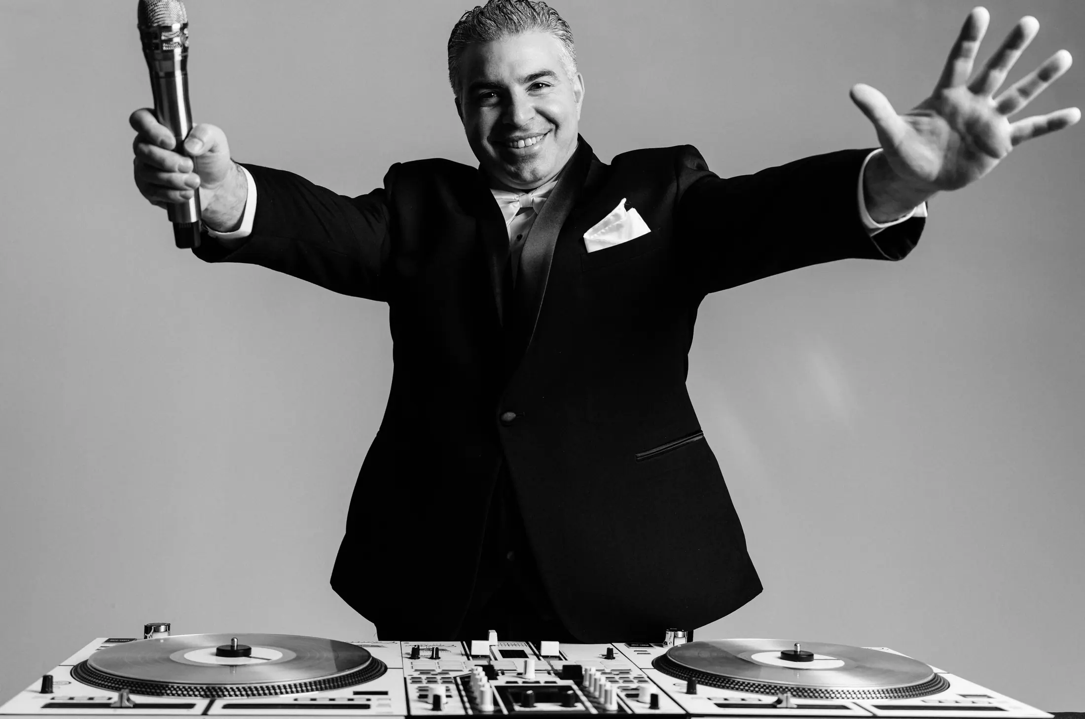 Pittsburgh wedding DJ Jonathan Mihellis with arms outstretched, holding a microphone behind a pair of turntables