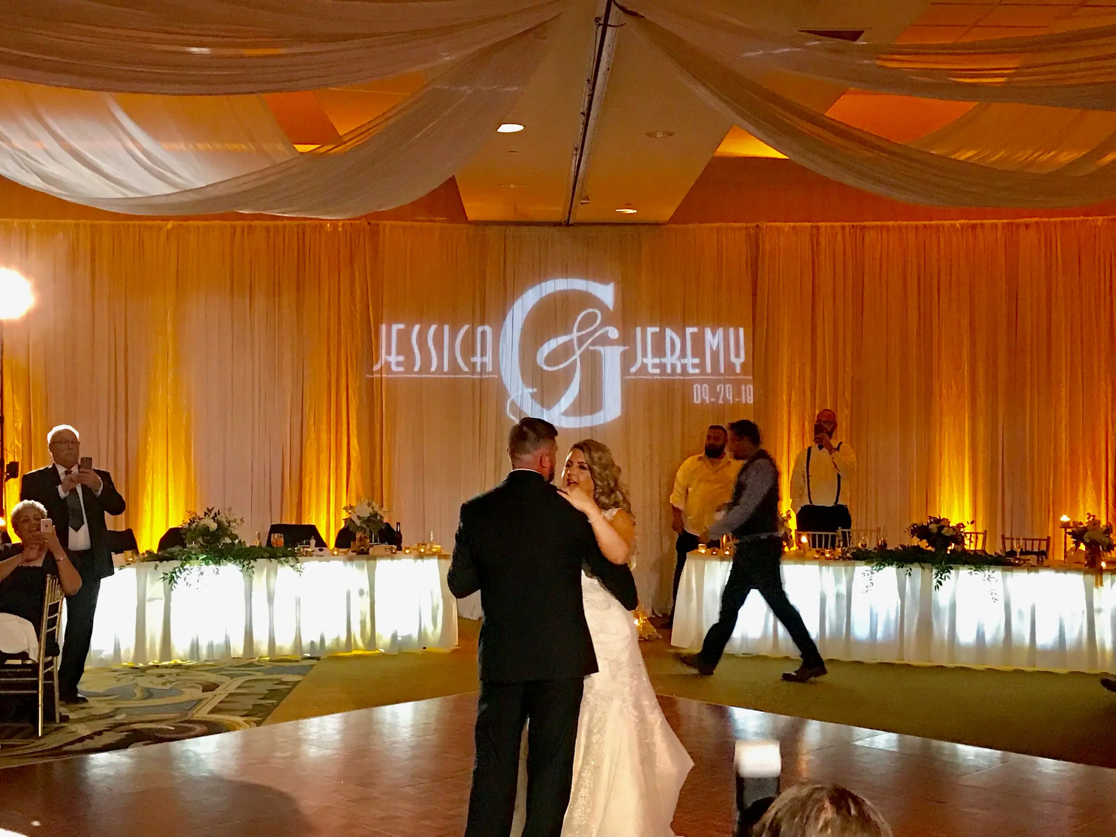 Couple’s first dance beneath a monogram projected onto a draped amber wall