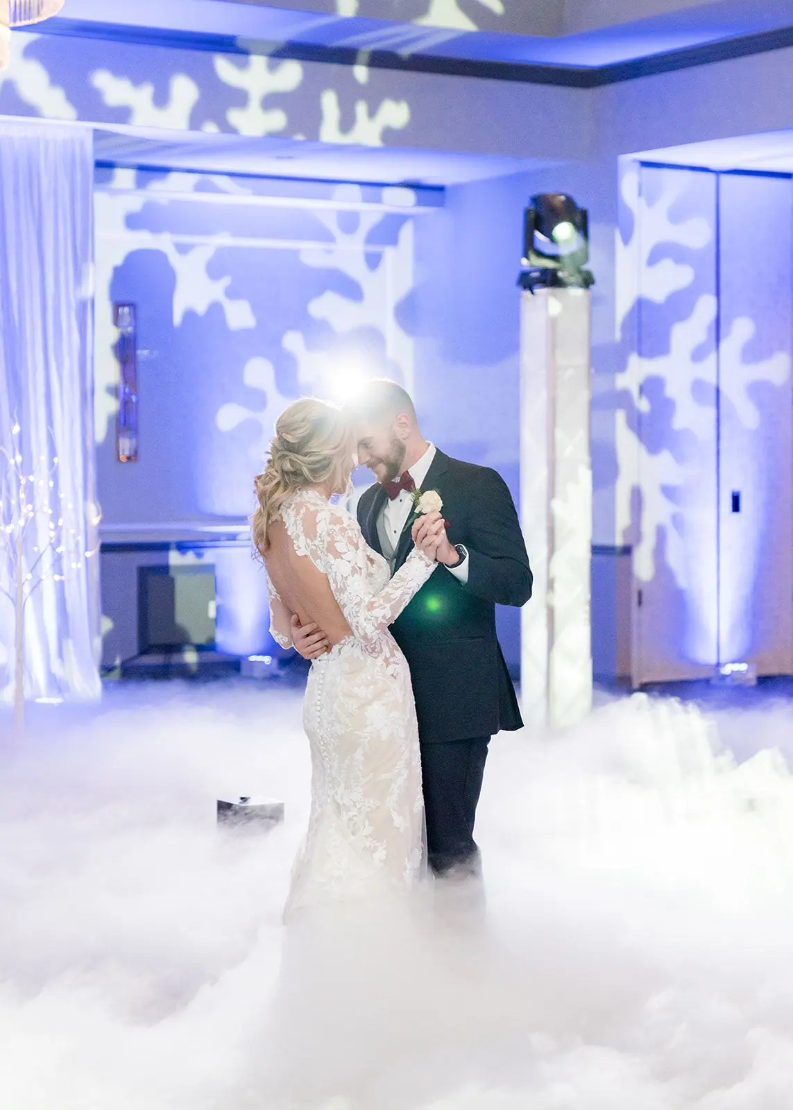Couple dancing on a cloud of fog under snowflake pattern lighting at their wedding