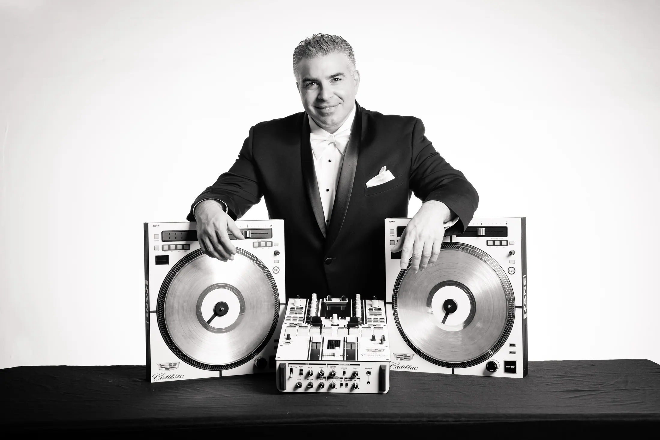 Jonathan Mihellis of Finest Events standing behind turntables in a black tuxedo