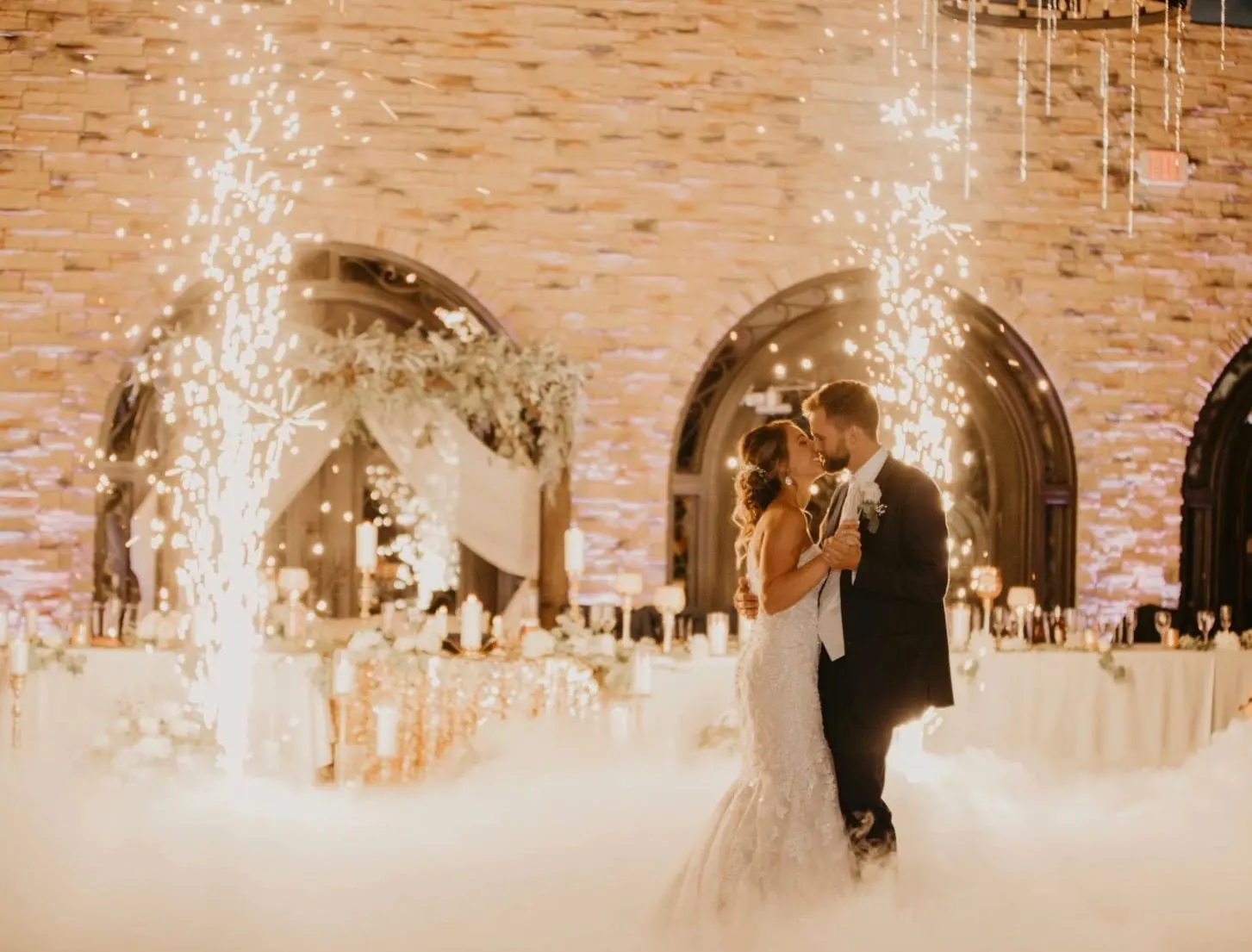 Couple’s first dance in a cloud of fog with sparkler fountains in a brick-walled venue
