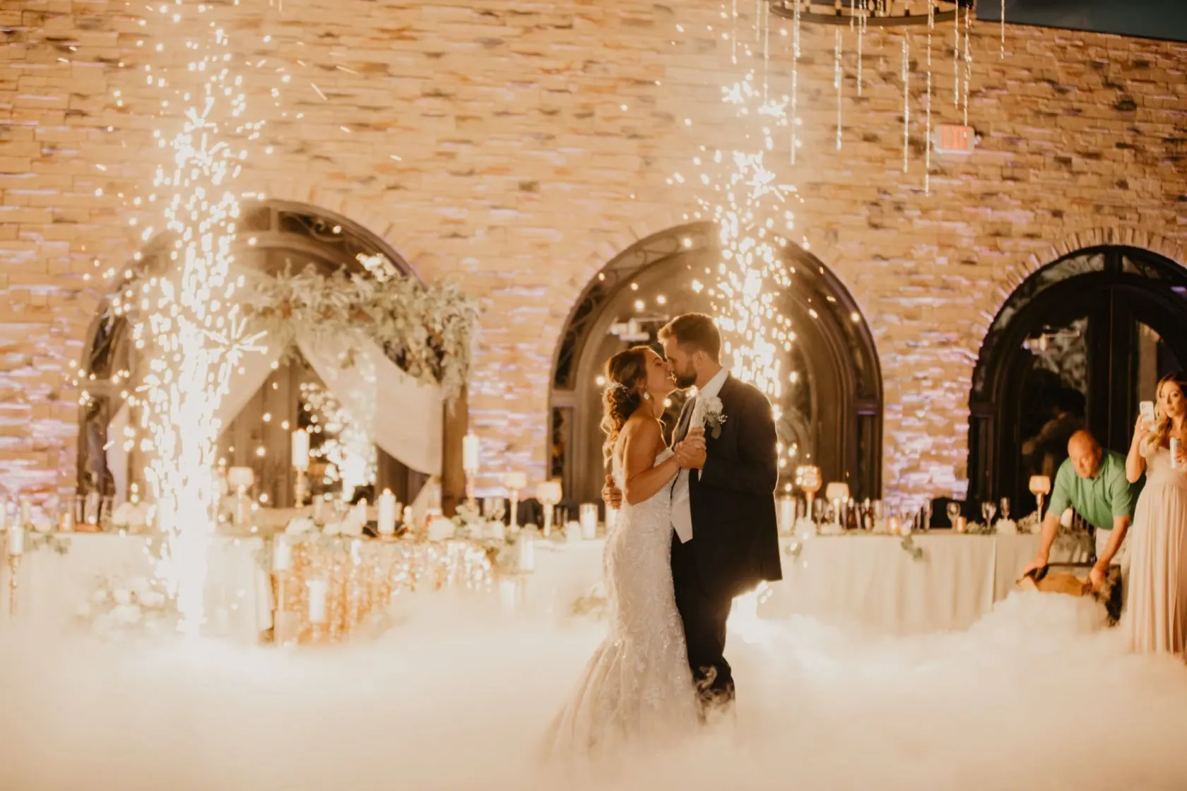 Couple’s first dance in a cloud of fog with sparkler fountains in a brick-walled venue